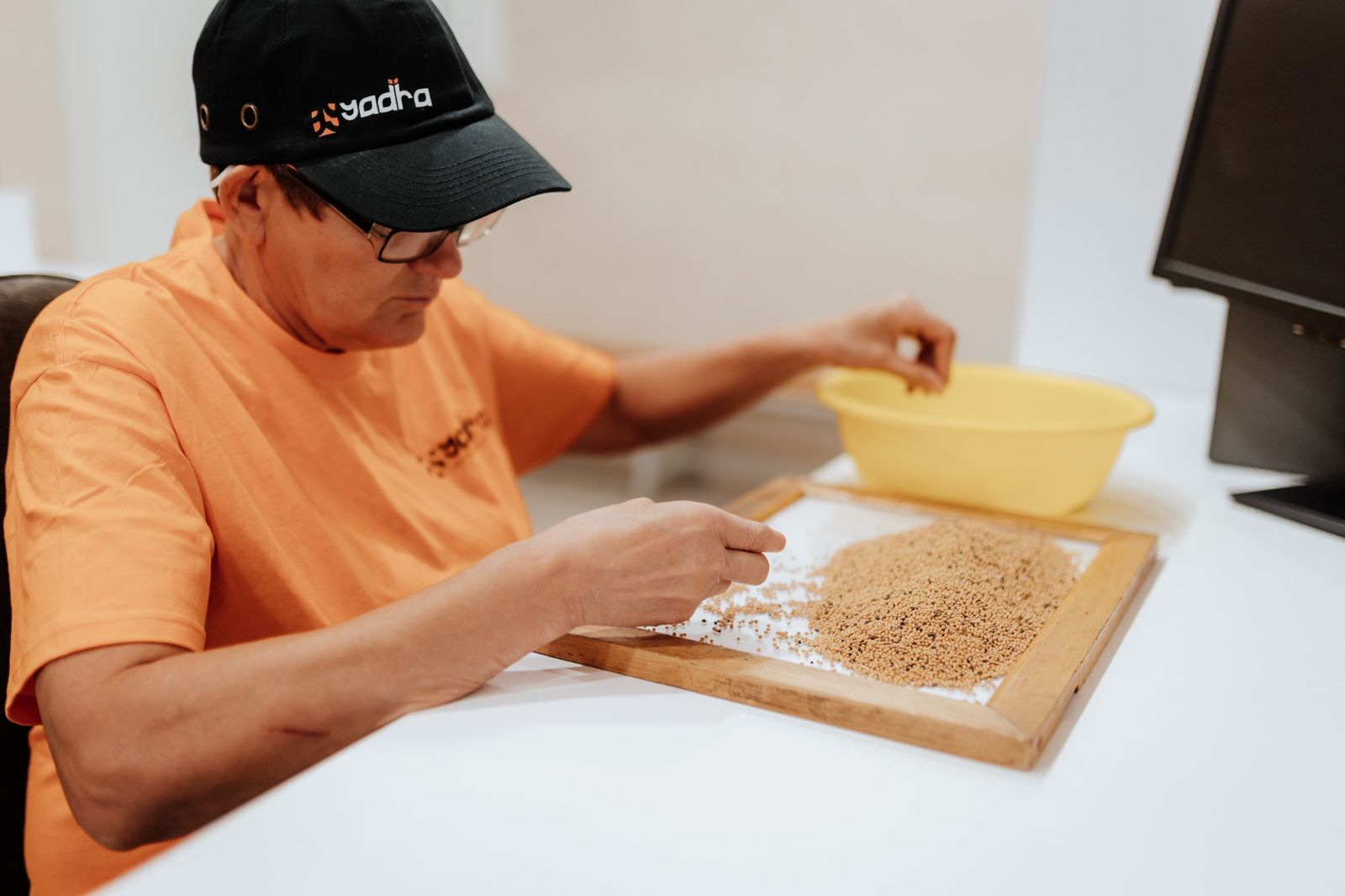 A Yadra worker in a branded cap sorting a tray of seeds by hand
